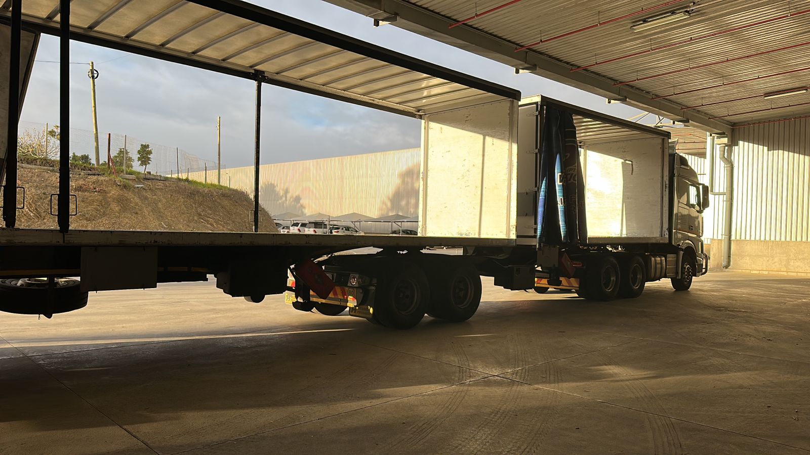 Tautliner trailer with curtains rolled open, parked under the warehouse canopy